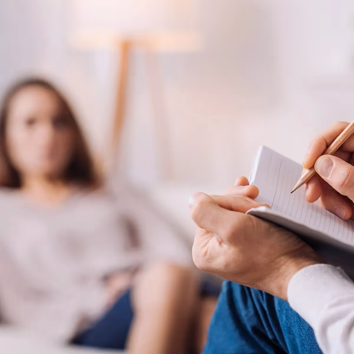 Psychotherapeut schreibt Notizen während der Therapiesitzung mit einer Patientin im Hintergrund.